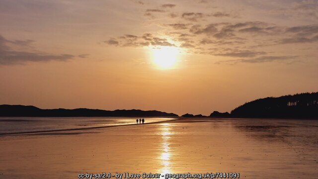Sunset at Llanddwyn Beach — warm amber light on the sand and water at the western end of the beach.