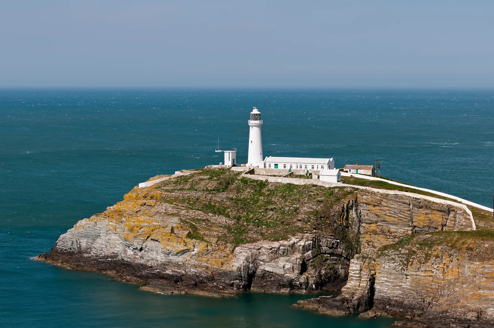 South Stack Lighthouse on its promontory seen across a deep rocky cove from the cliffs of Holy Island.